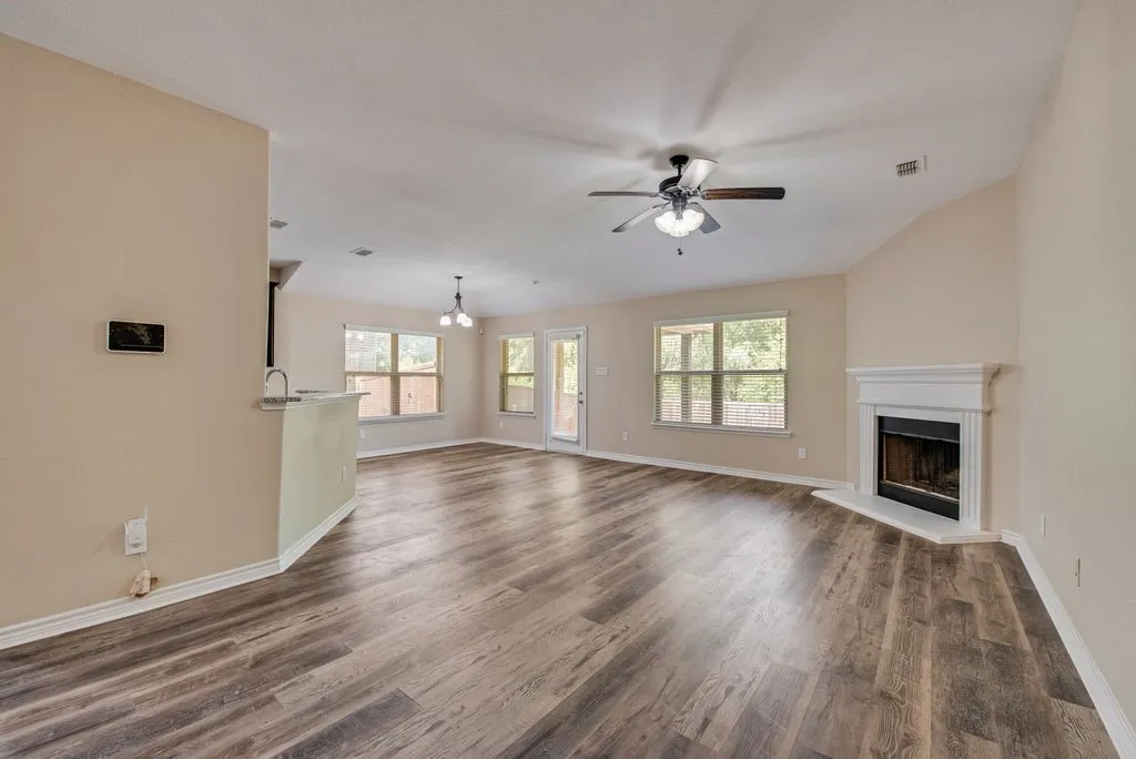 Open-concept living space featuring wood-finish flooring, a white mantel fireplace, and a ceiling fan with integrated lighting