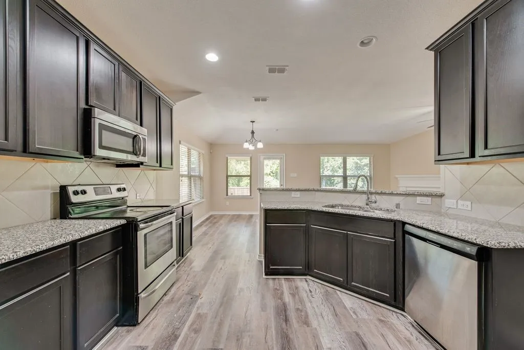 Open-concept kitchen featuring wood-finish flooring, dark wood cabinetry, stainless steel appliances, and granite countertops