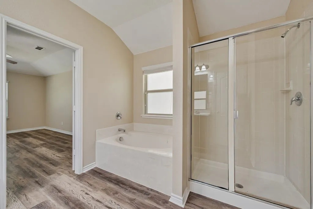 Bathroom featuring a soaking tub with an integrated shower, glass-enclosed shower, wood-finish flooring, and a vaulted ceiling