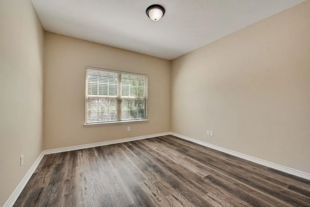 Room featuring wood-finish flooring, neutral wall tones, a double window with blinds, white trim, and a ceiling-mounted light fixture