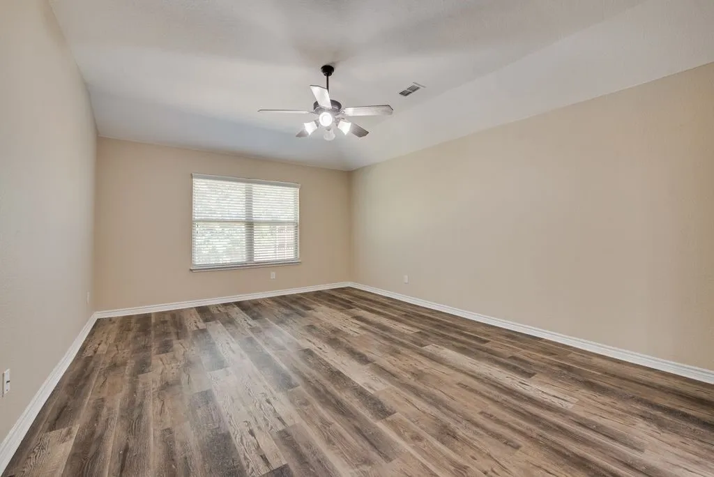 Spacious room featuring wood-finish flooring, vaulted ceiling, and a ceiling fan with light fixture