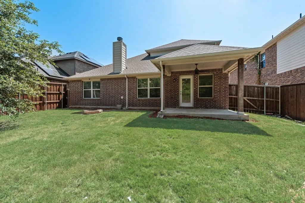 Expansive backyard featuring a covered patio, red brick exterior, a substantial chimney, and privacy fencing