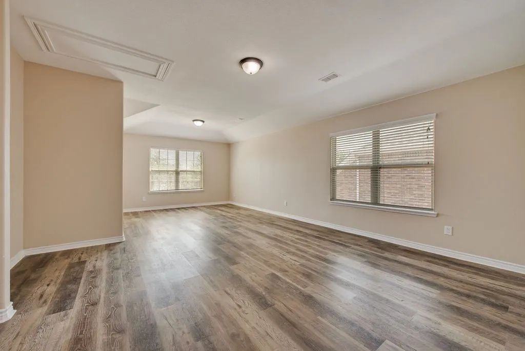 Spacious room featuring wood-finish flooring, two windows with blinds, a neutral wall color, and a ceiling-mounted light fixture