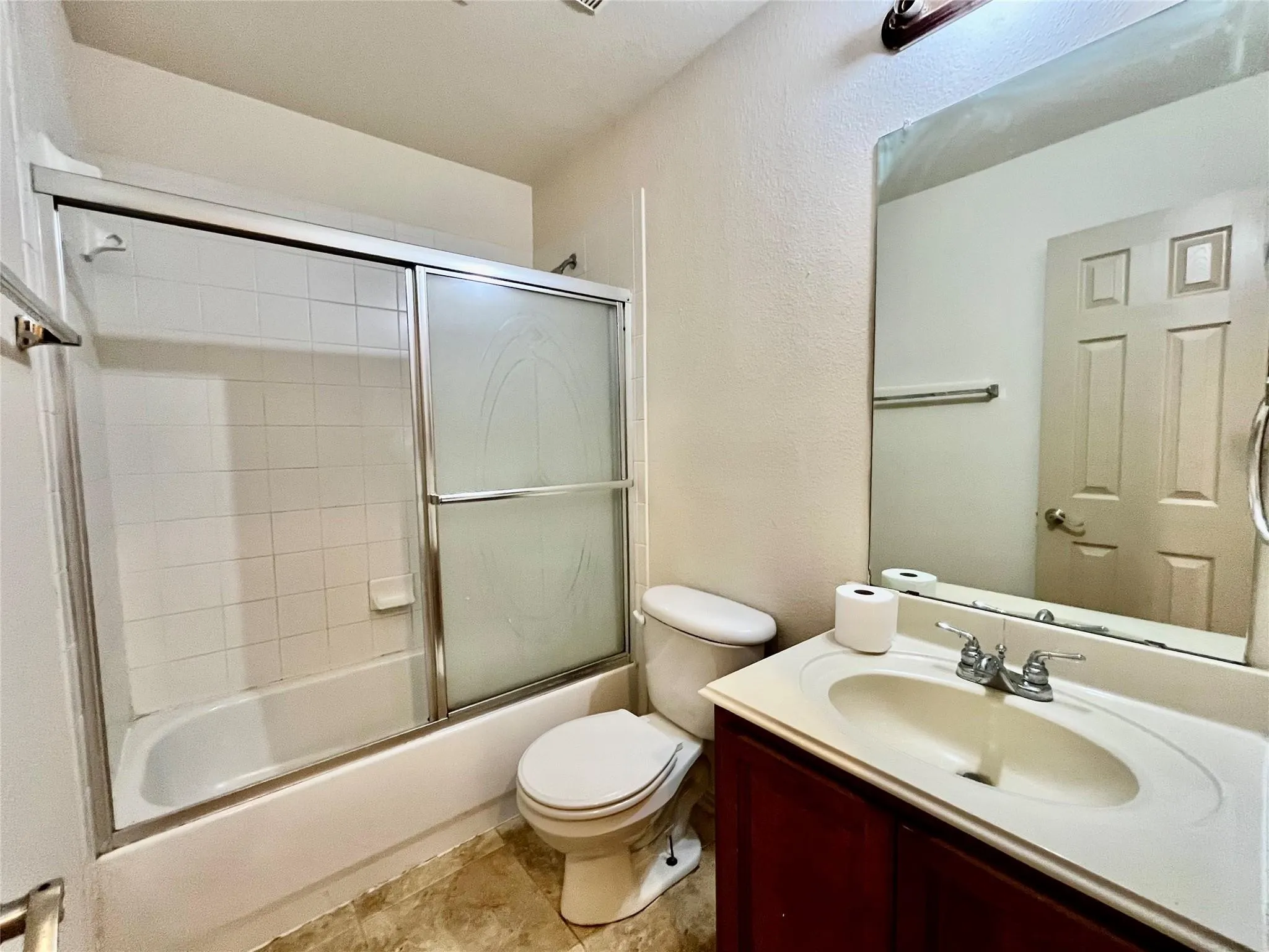 Bathroom with tub/shower, vanity, toilet, and tile flooring.