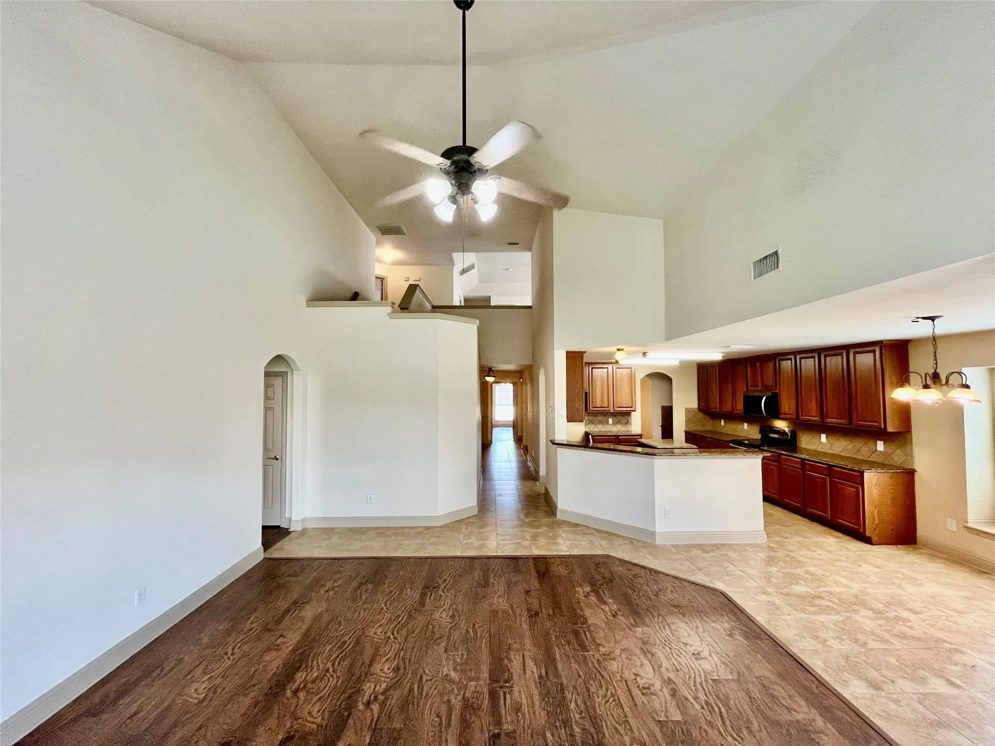 Open living area with wood flooring, ceiling fan, and kitchen access