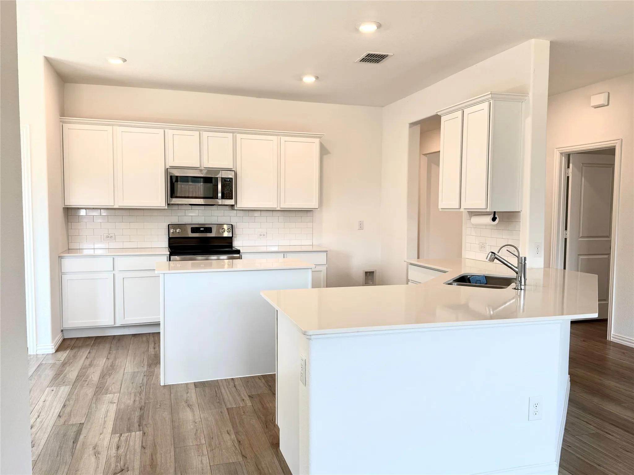 Open-concept kitchen featuring wood-finish flooring, white cabinetry, a subway tile backsplash, and stainless steel appliances