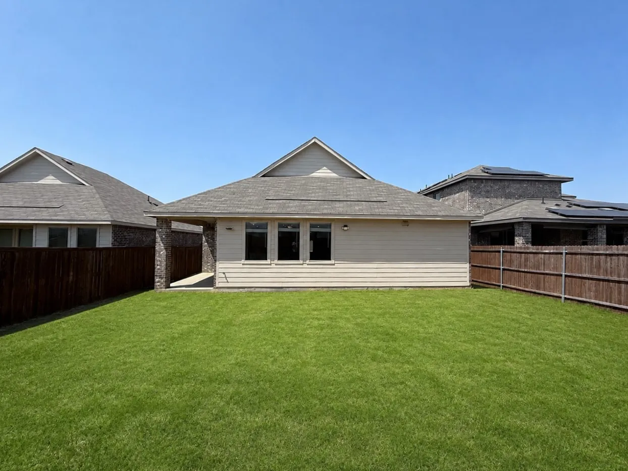 Expansive backyard featuring a manicured lawn, wood fencing, and a covered patio area with stone pillars
