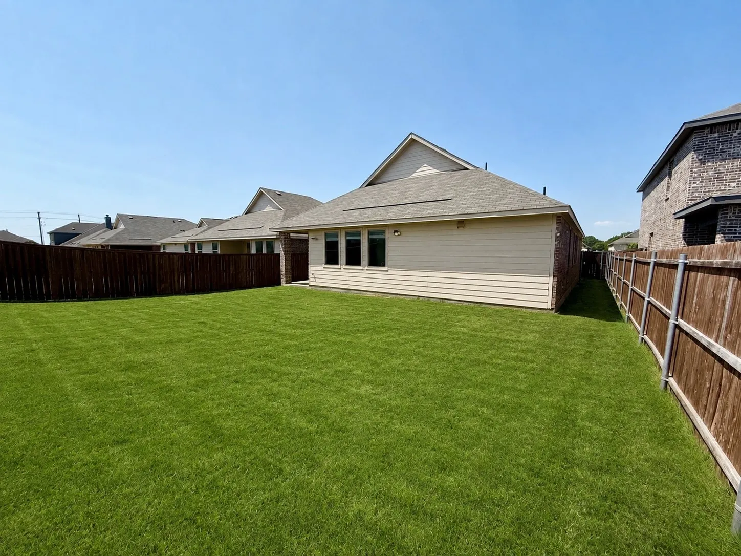 Expansive backyard featuring a manicured lawn, a full wood fence, and a neutral-toned siding exterior with multiple windows