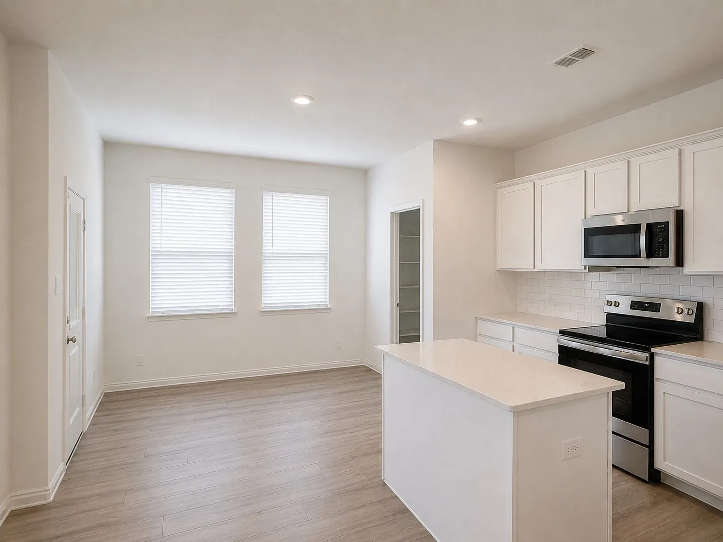 Open-concept kitchen featuring white cabinetry, stainless steel appliances, a center island with a light-toned countertop, and wood-finish flooring