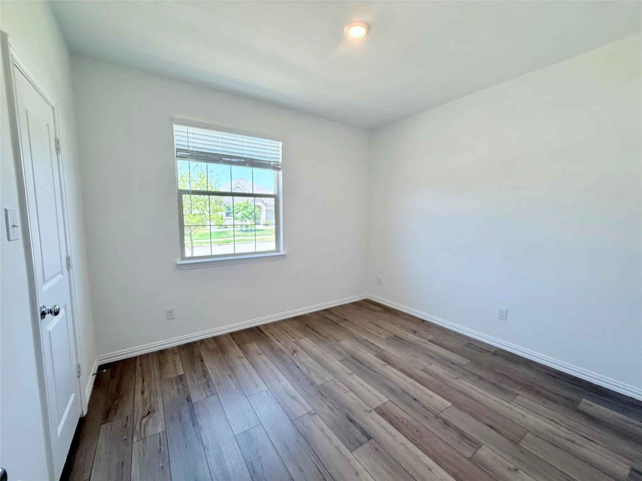 Recessed ceiling lighting, wood-finish flooring, window with blinds, white trim, and a paneled door
