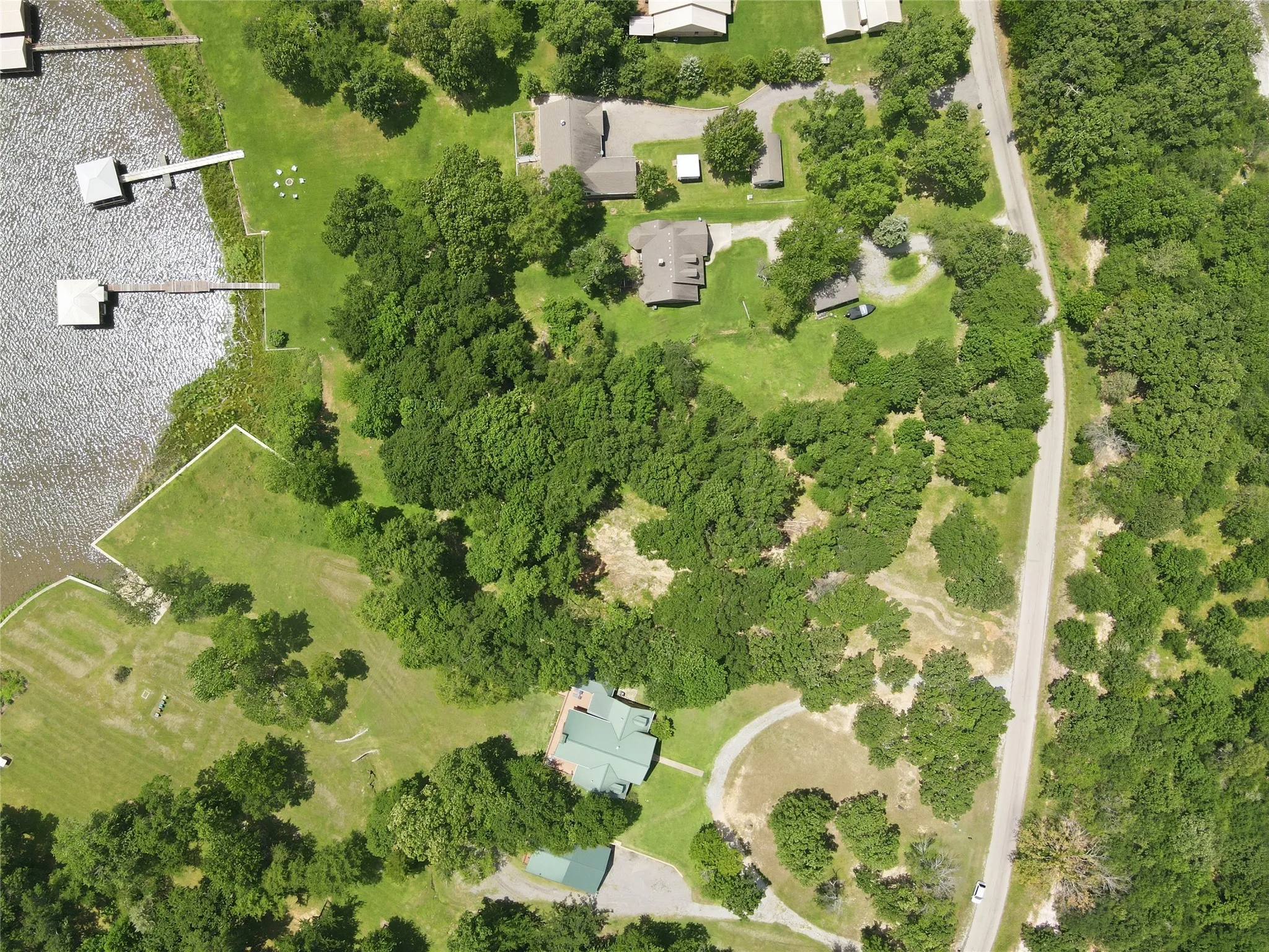 Waterfront property featuring multiple docks, extensive tree coverage, and a paved road