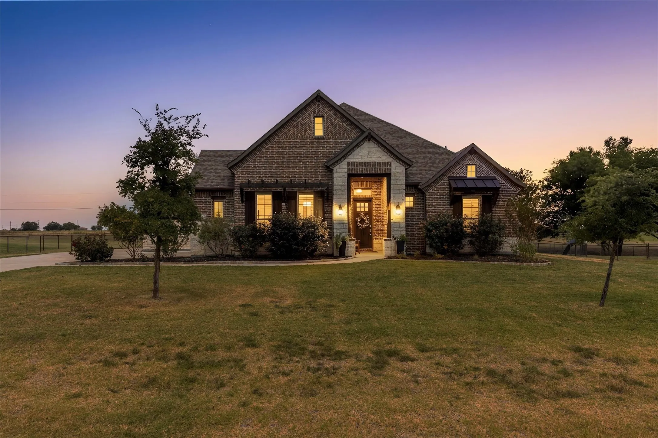 Twilight front exterior of the main home, with a stone and brick facade, a covered entry, and a large front lawn.