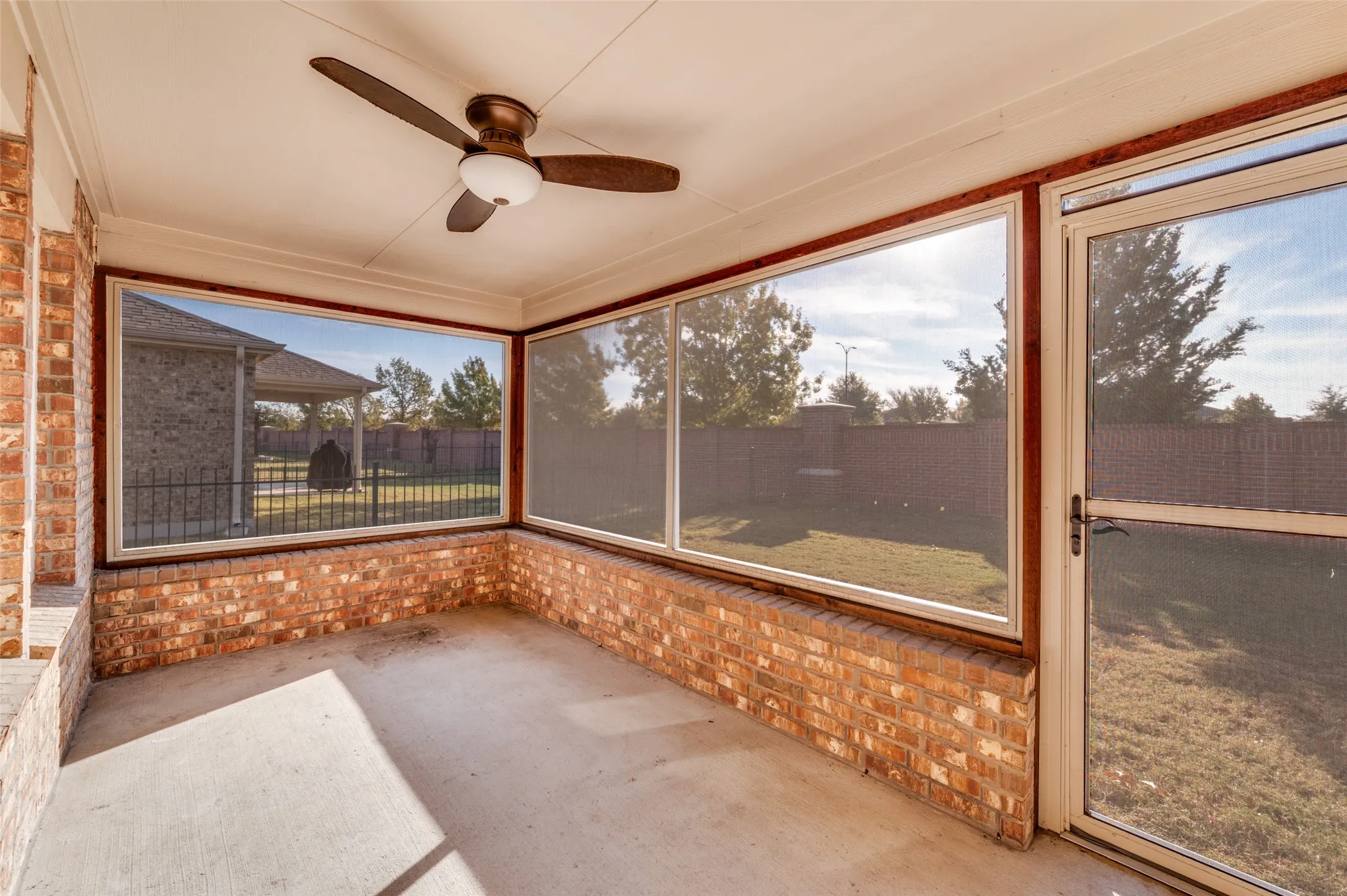 Screened-in patio featuring a ceiling fan, brick half-walls, and a concrete floor