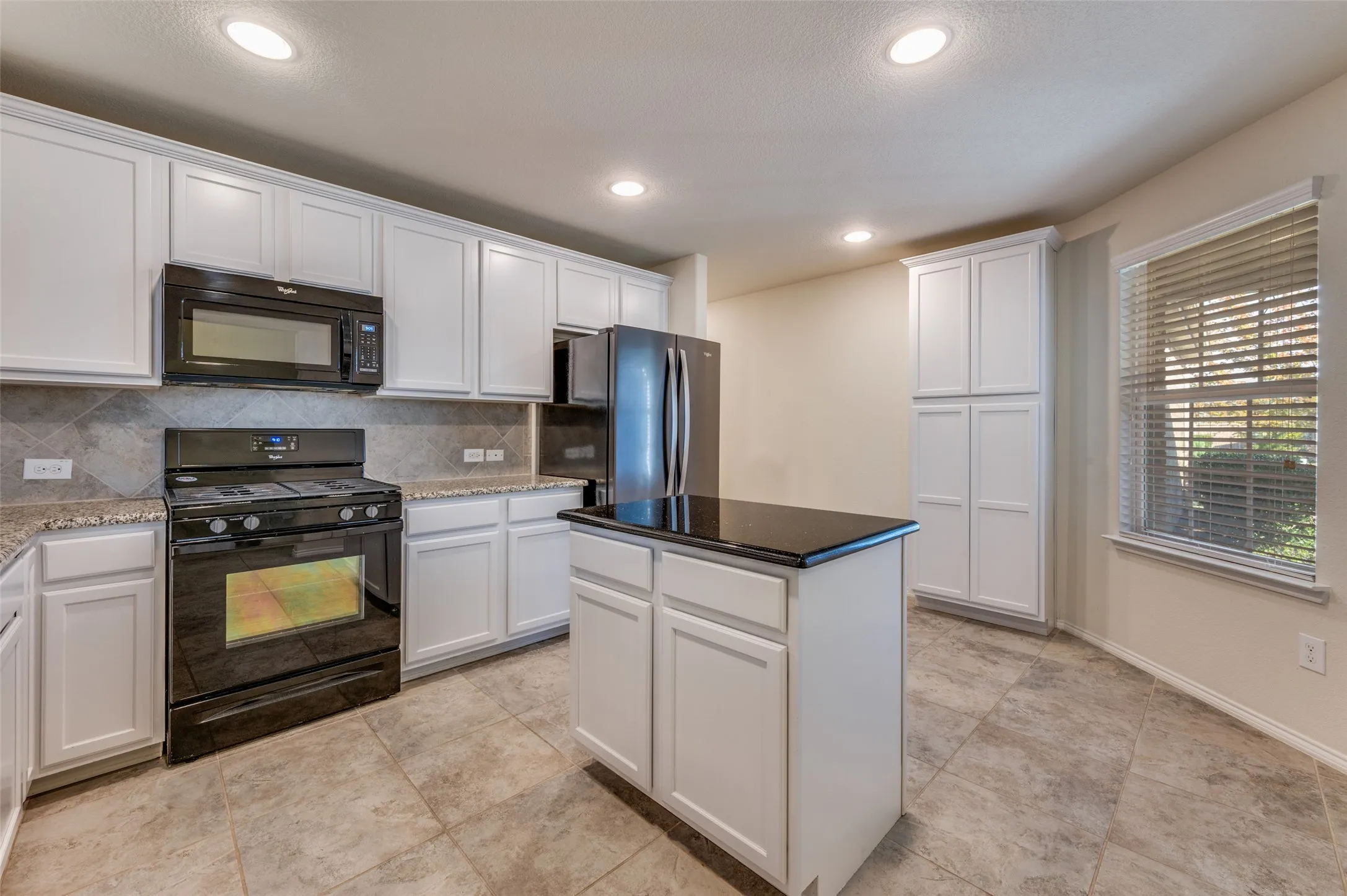 White cabinetry, granite countertops, tile flooring, built-in appliances, and a central island