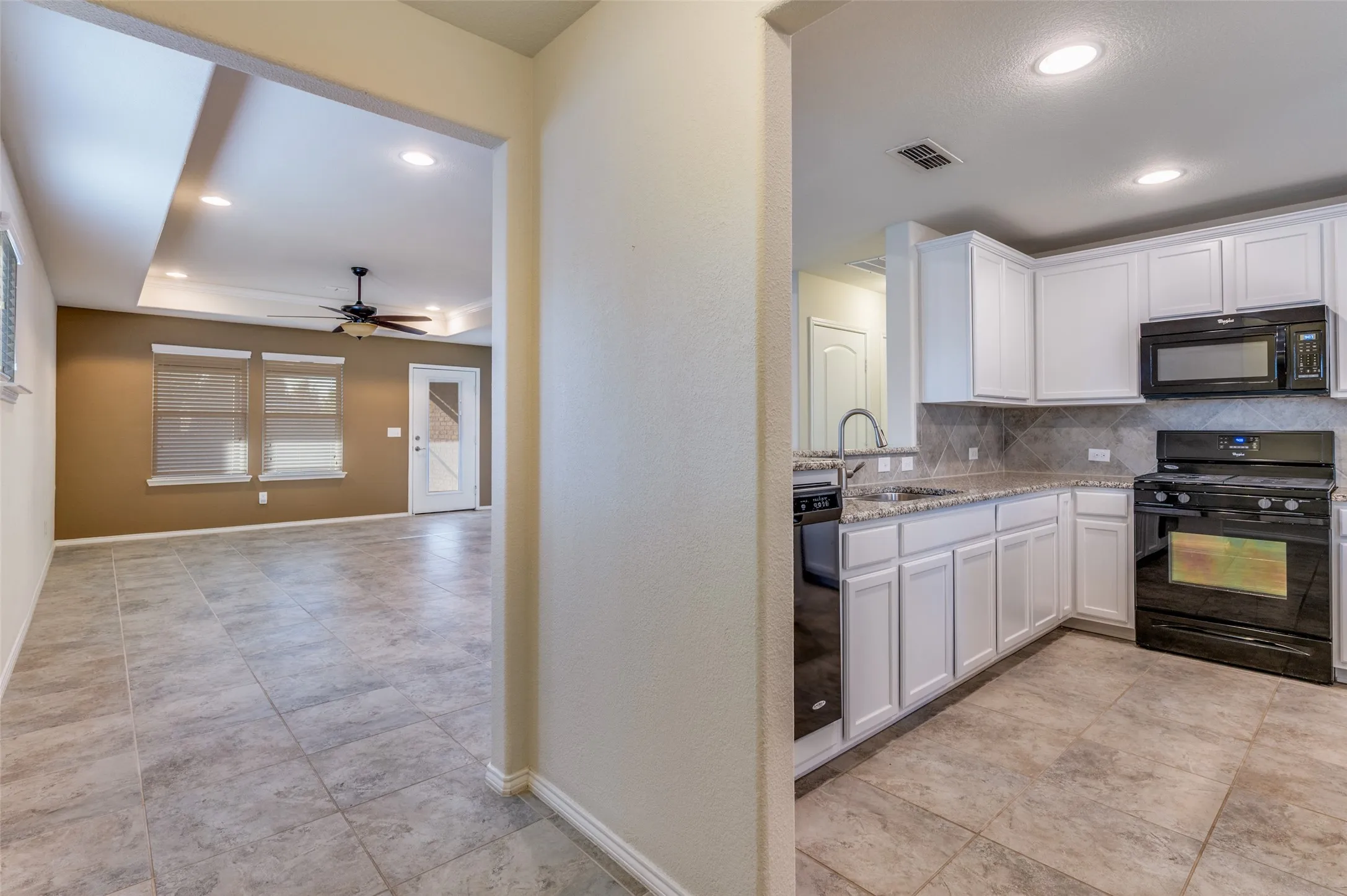 Kitchen featuring white cabinetry, light-toned countertops, a tile backsplash, and black appliances
