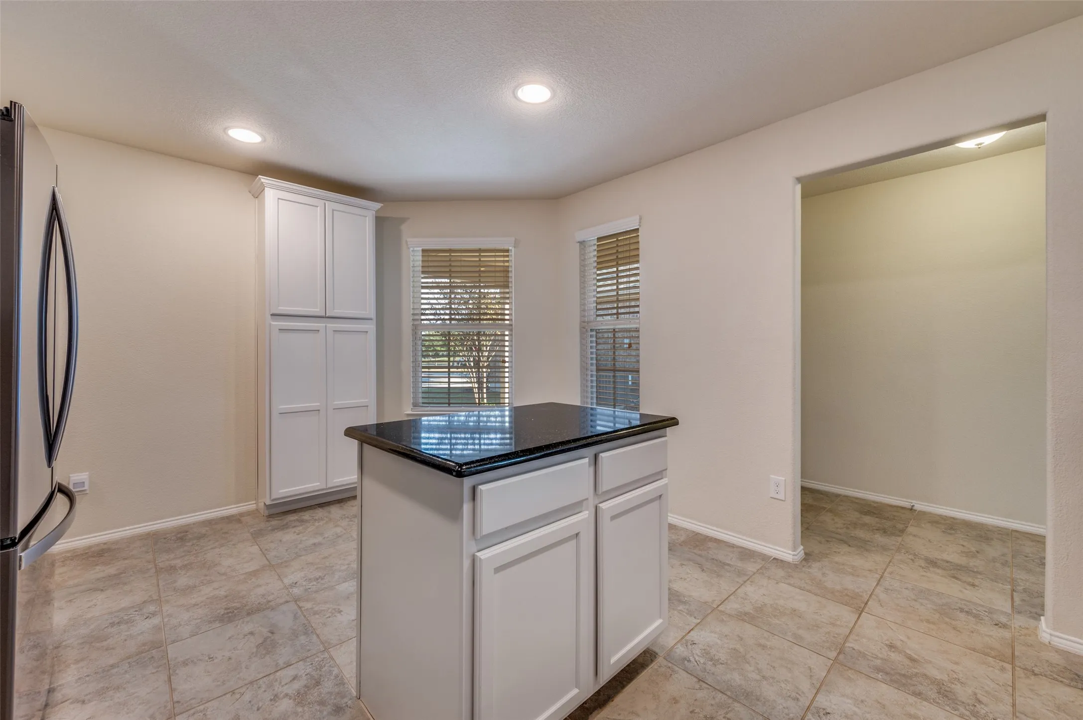 Kitchen featuring a central island with a dark countertop, white cabinetry, recessed lighting, and tile flooring