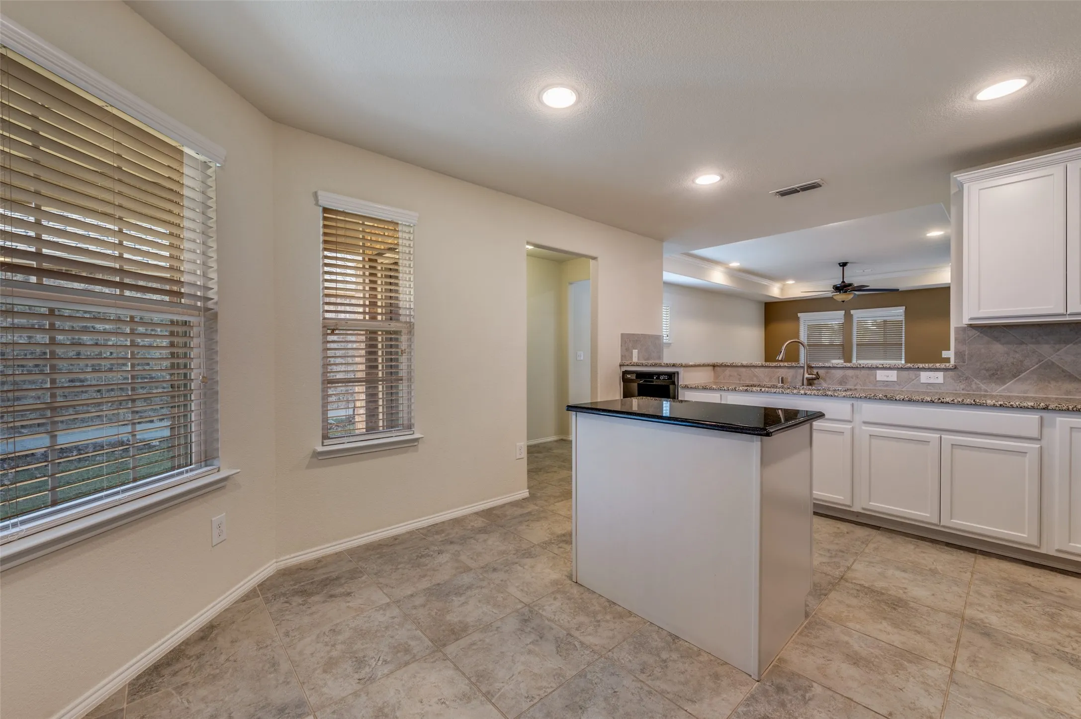 Kitchen featuring white cabinetry, stone countertops, a tile backsplash, and a central island with a dark countertop