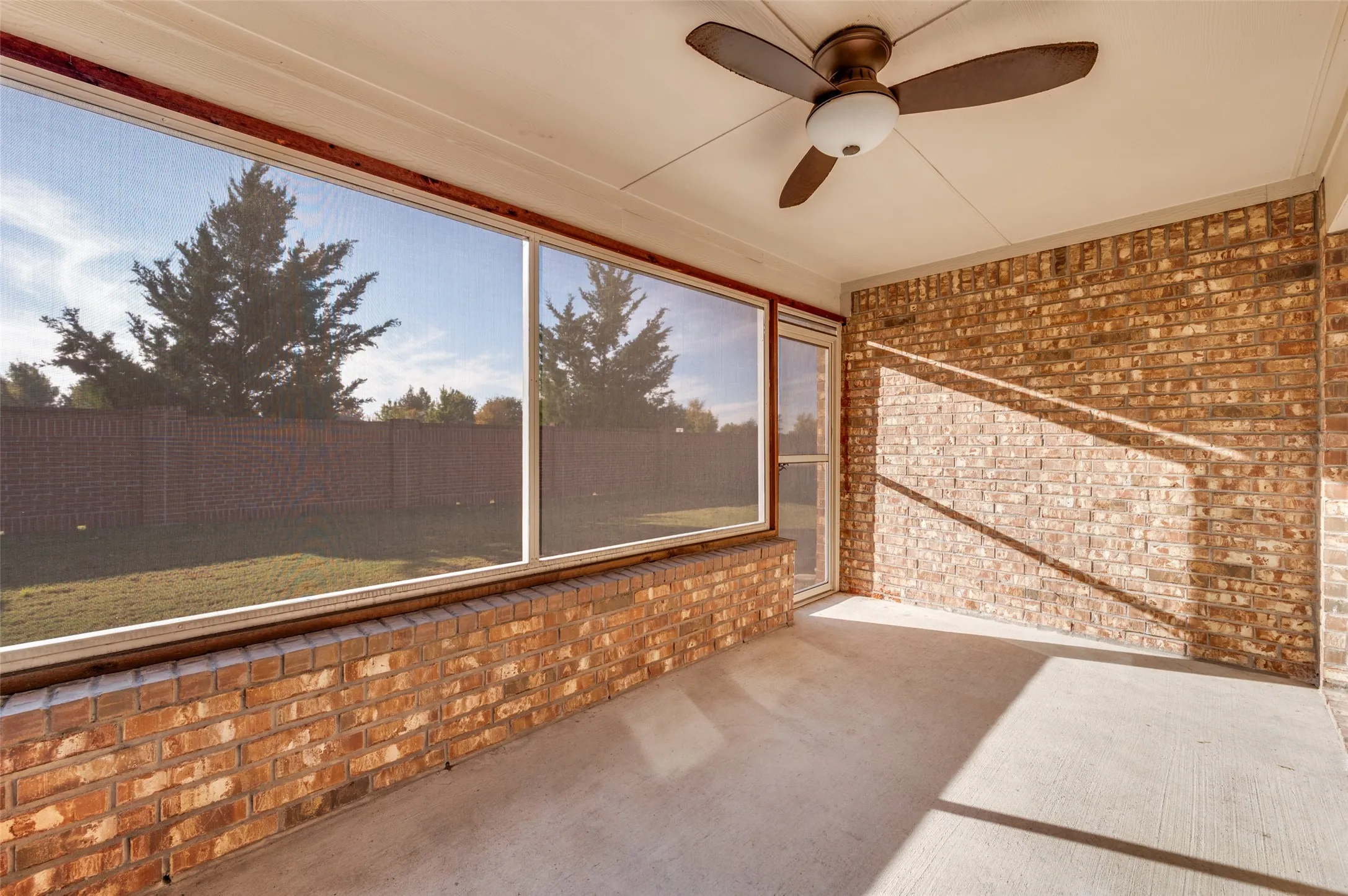 Screened patio featuring a ceiling fan, brick walls, and concrete flooring