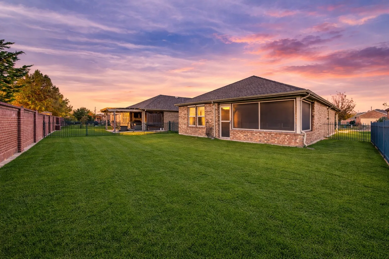 Expansive backyard with a manicured lawn, brick perimeter wall, and black metal fencing