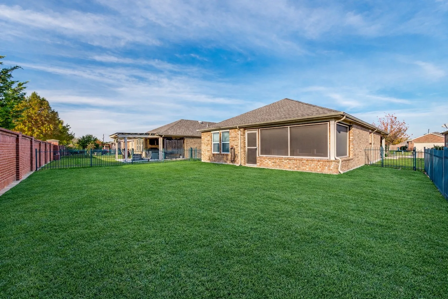 Expansive green lawn, brick exterior, screened-in porch, privacy fencing, and extended patio