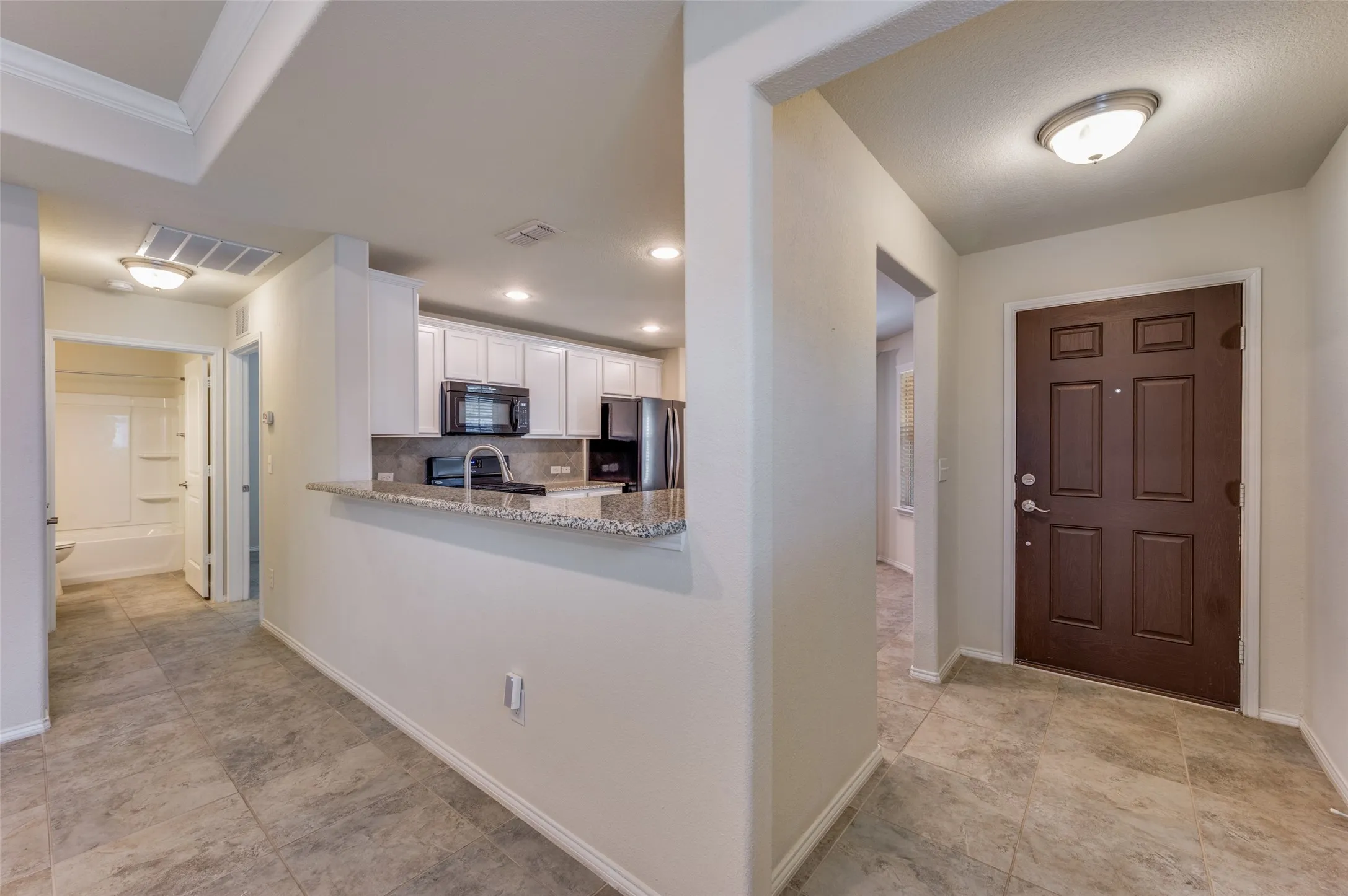 Tiled flooring throughout, kitchen with white cabinetry and granite countertops, built-in microwave, and a paneled front door