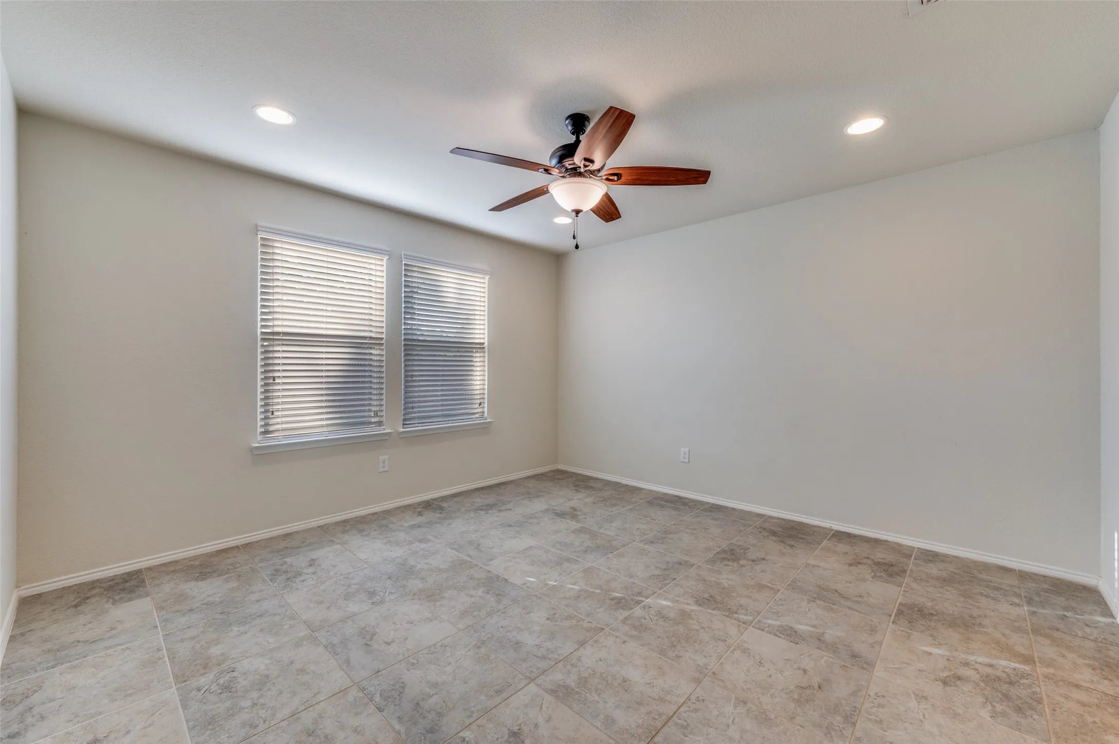 Recessed lighting, ceiling fan with light fixture, two windows with blinds, and large format tile flooring