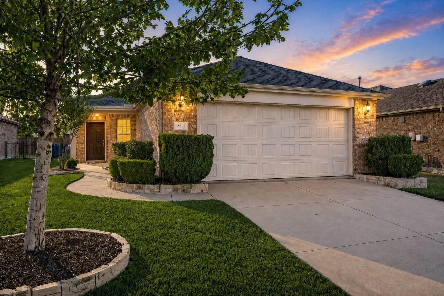 Brick facade home featuring a concrete driveway, attached garage, curved concrete walkway, and decorative landscaping