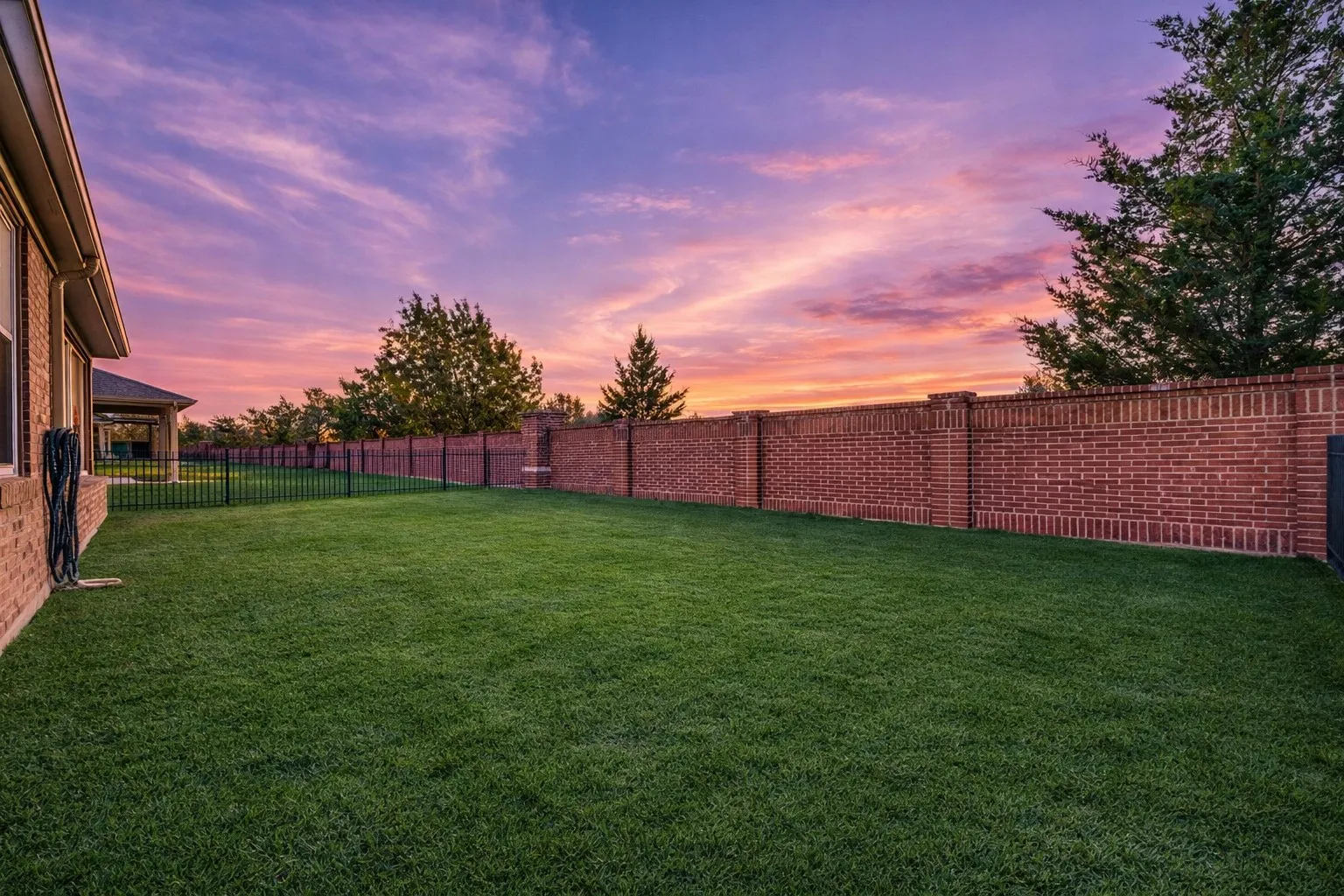 Expansive lawn area with a full brick privacy fence and an additional black metal fence