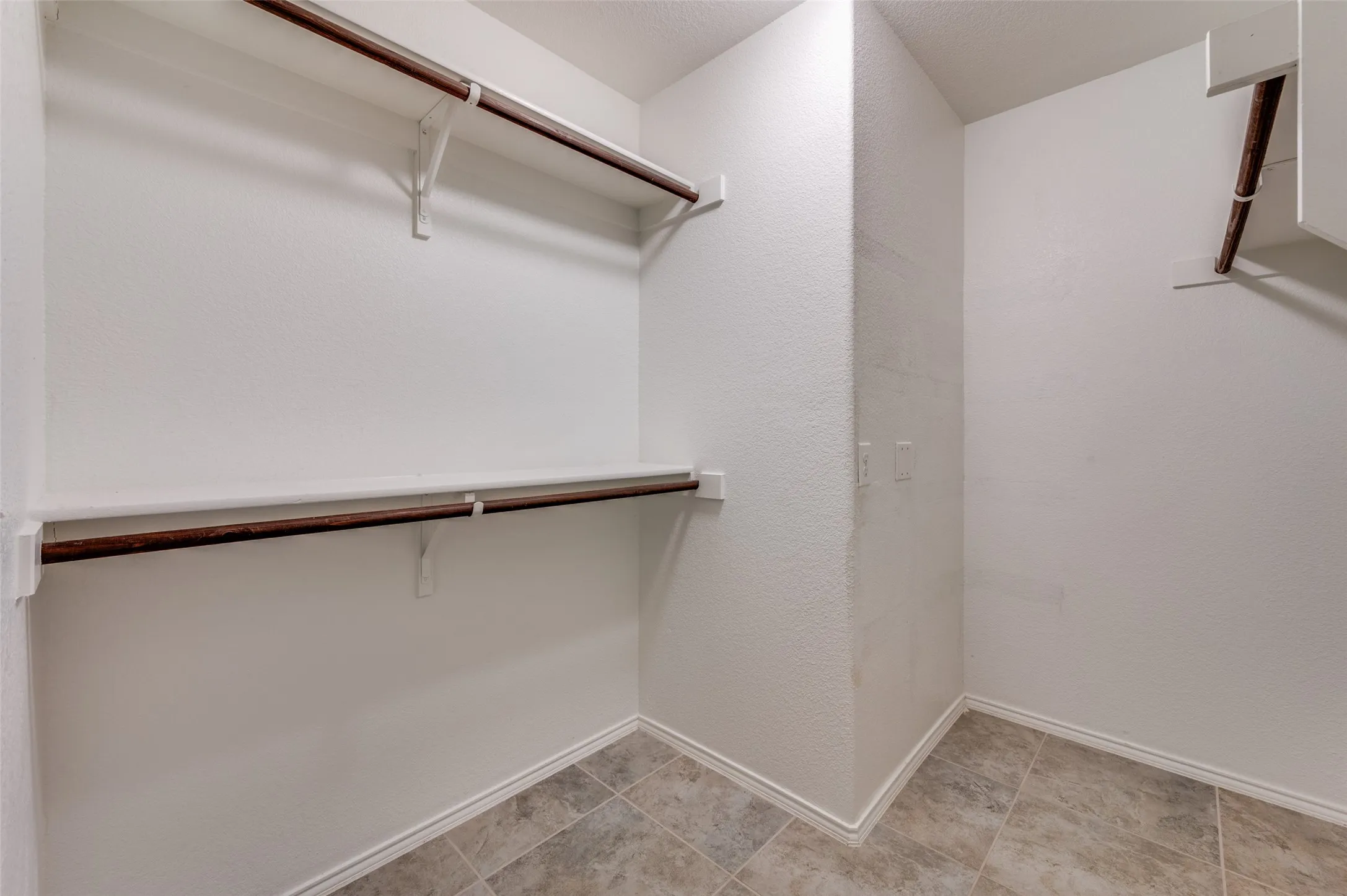 Walk-in closet featuring white painted walls, wood-finish shelving, and tiled flooring