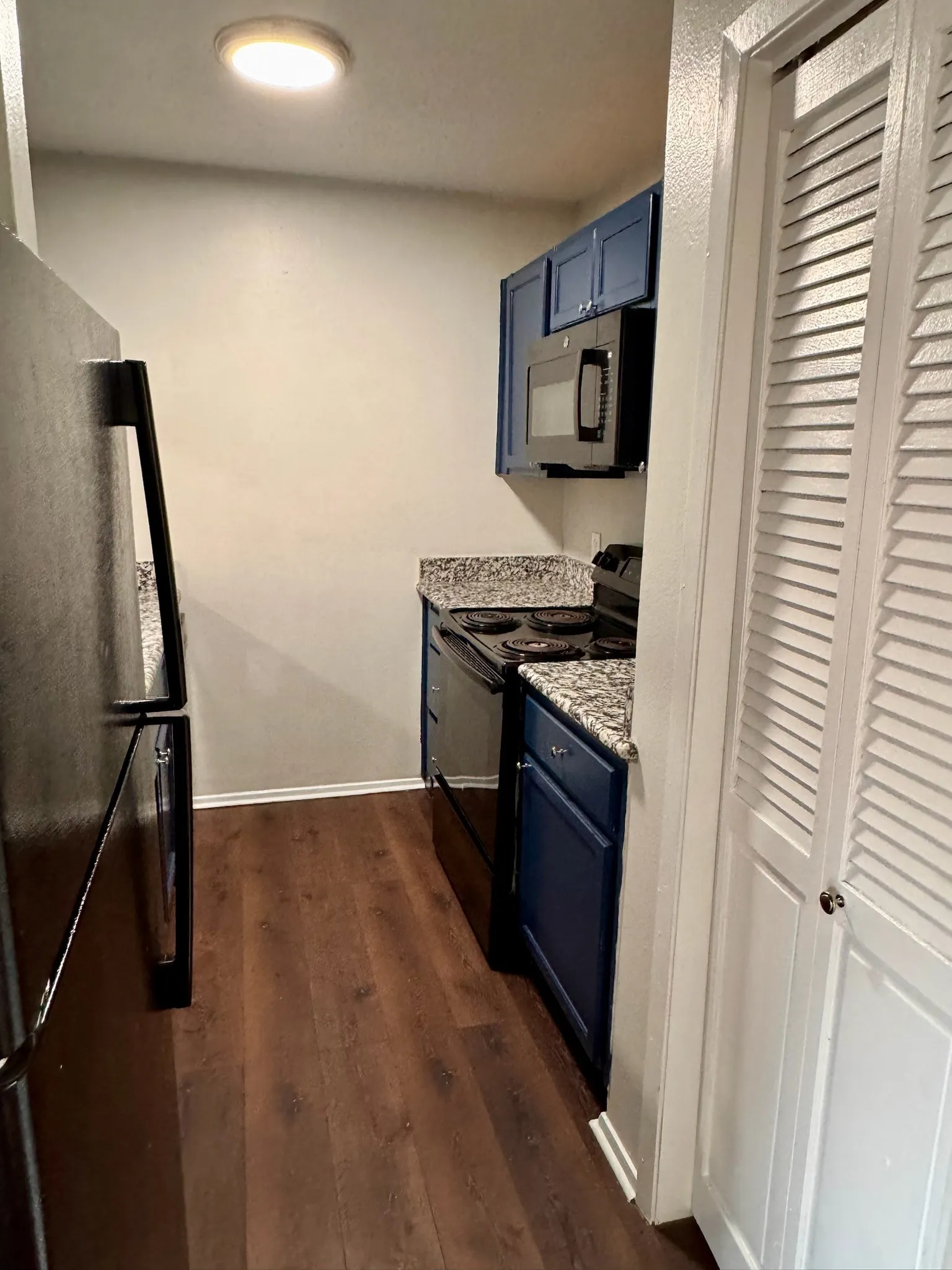 Kitchen featuring wood-finish flooring, blue cabinetry, a stainless steel microwave, a black electric range, and a black refrigerator