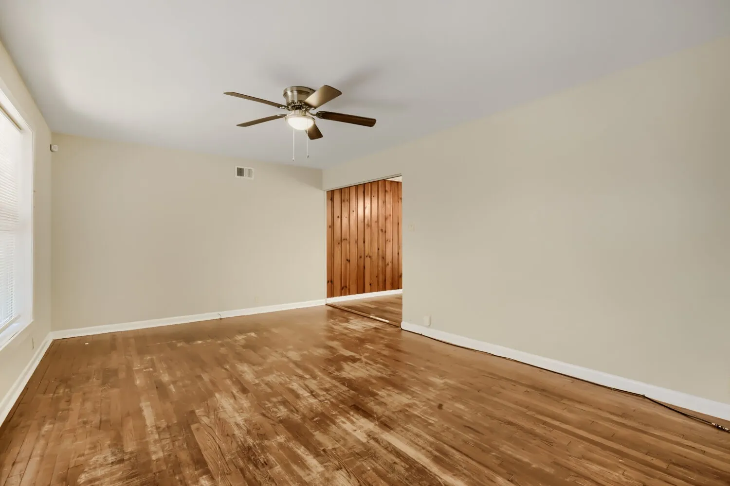 Recessed window with blinds, wood-finish flooring, ceiling fan with integrated lighting, and a wood-paneled accent wall