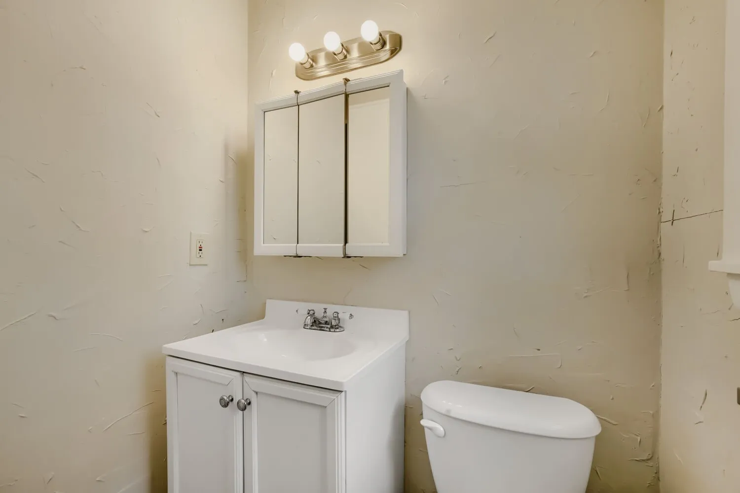 Clean and functional bathroom featuring a white vanity with dual cabinet doors, white porcelain sink, chrome faucet fixtures, and a toilet