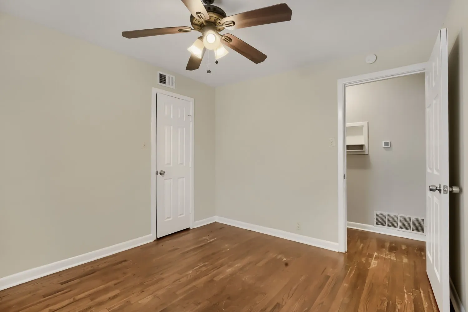 Spacious bedroom showcasing gleaming wood-finish flooring, neutral wall finishes, and abundant natural light
