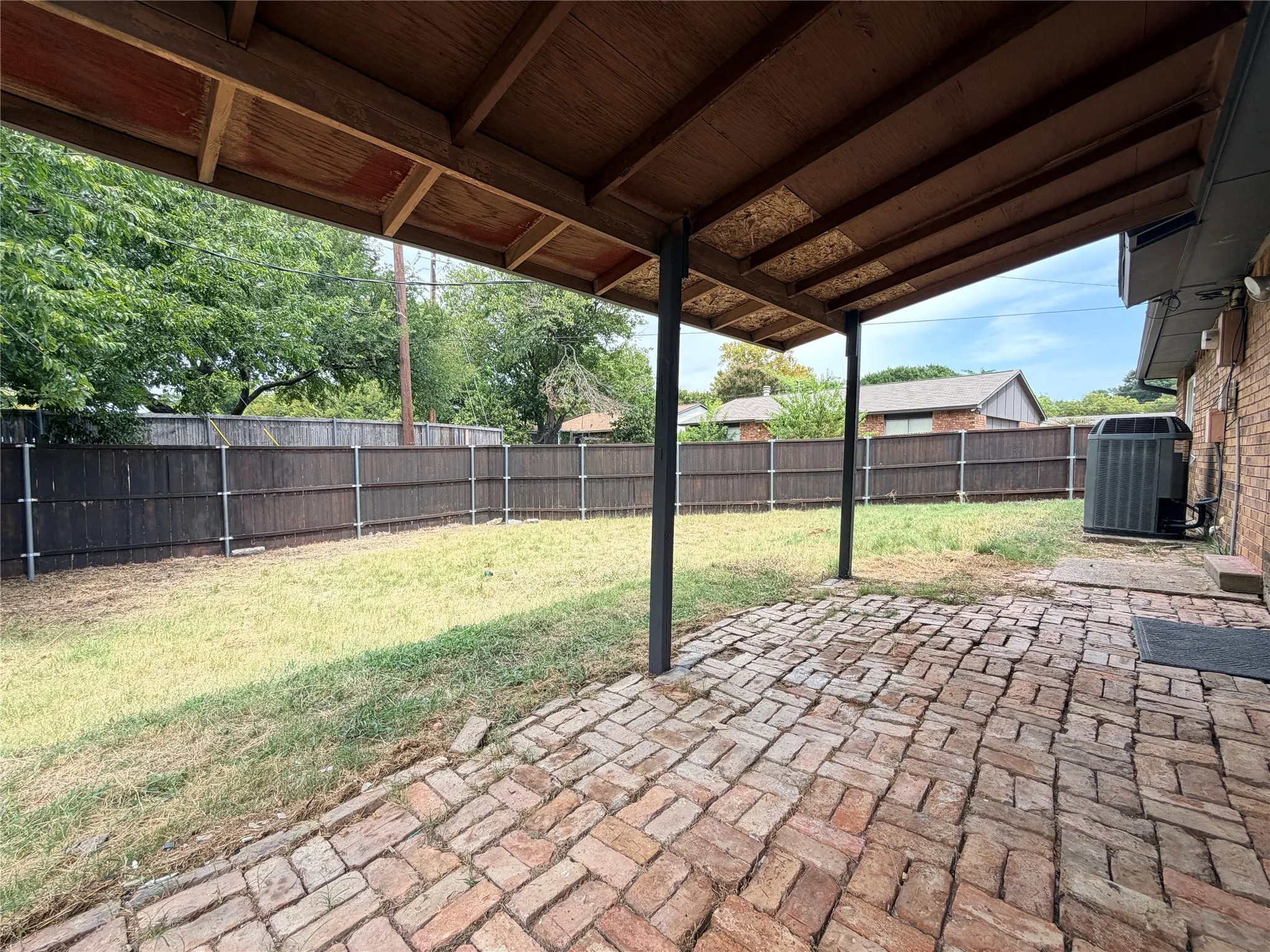 Covered patio with brick pavers, wood privacy fencing, and a grassy yard area