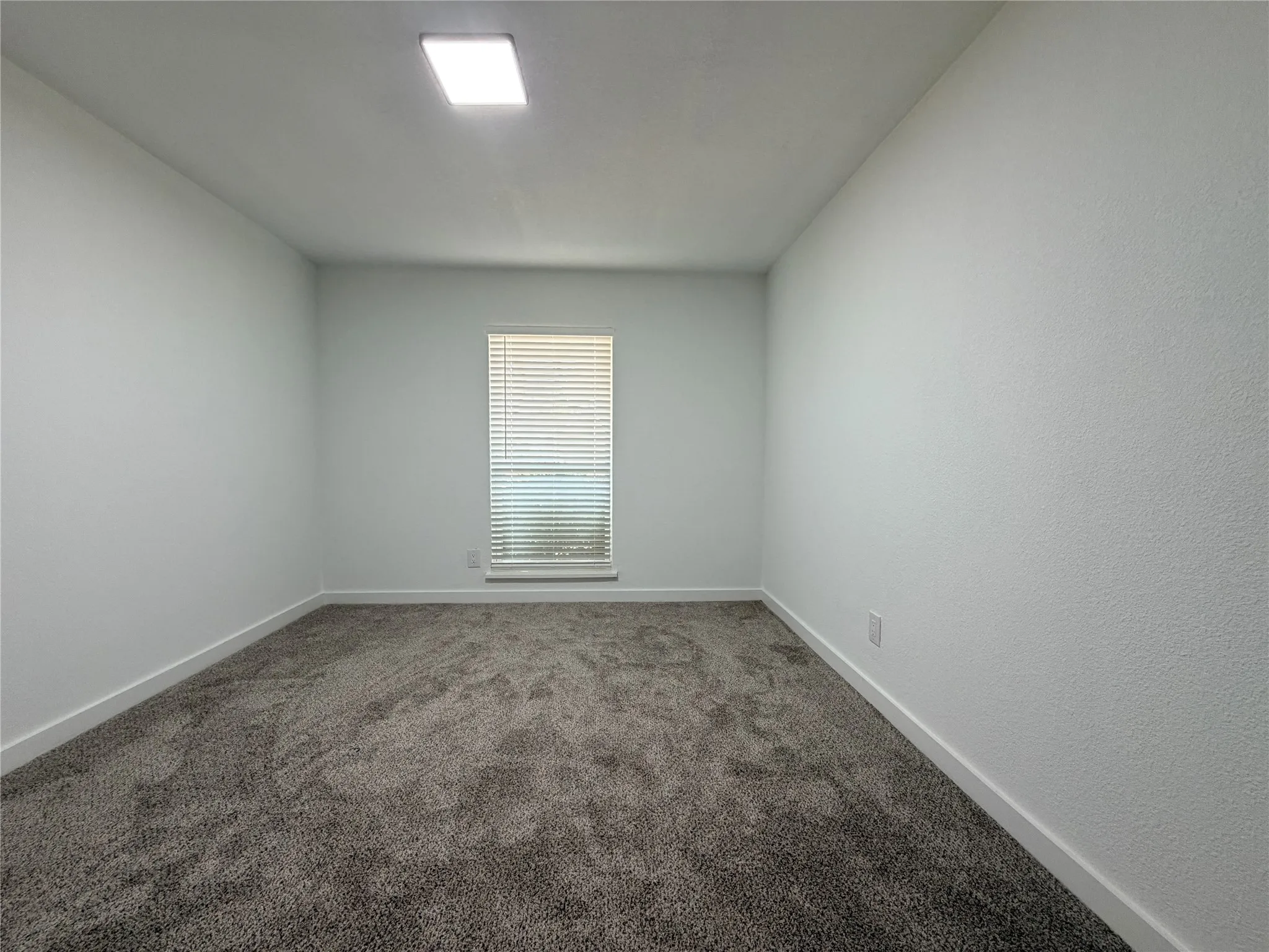Recessed ceiling light, textured walls, window with blinds, and neutral carpeting