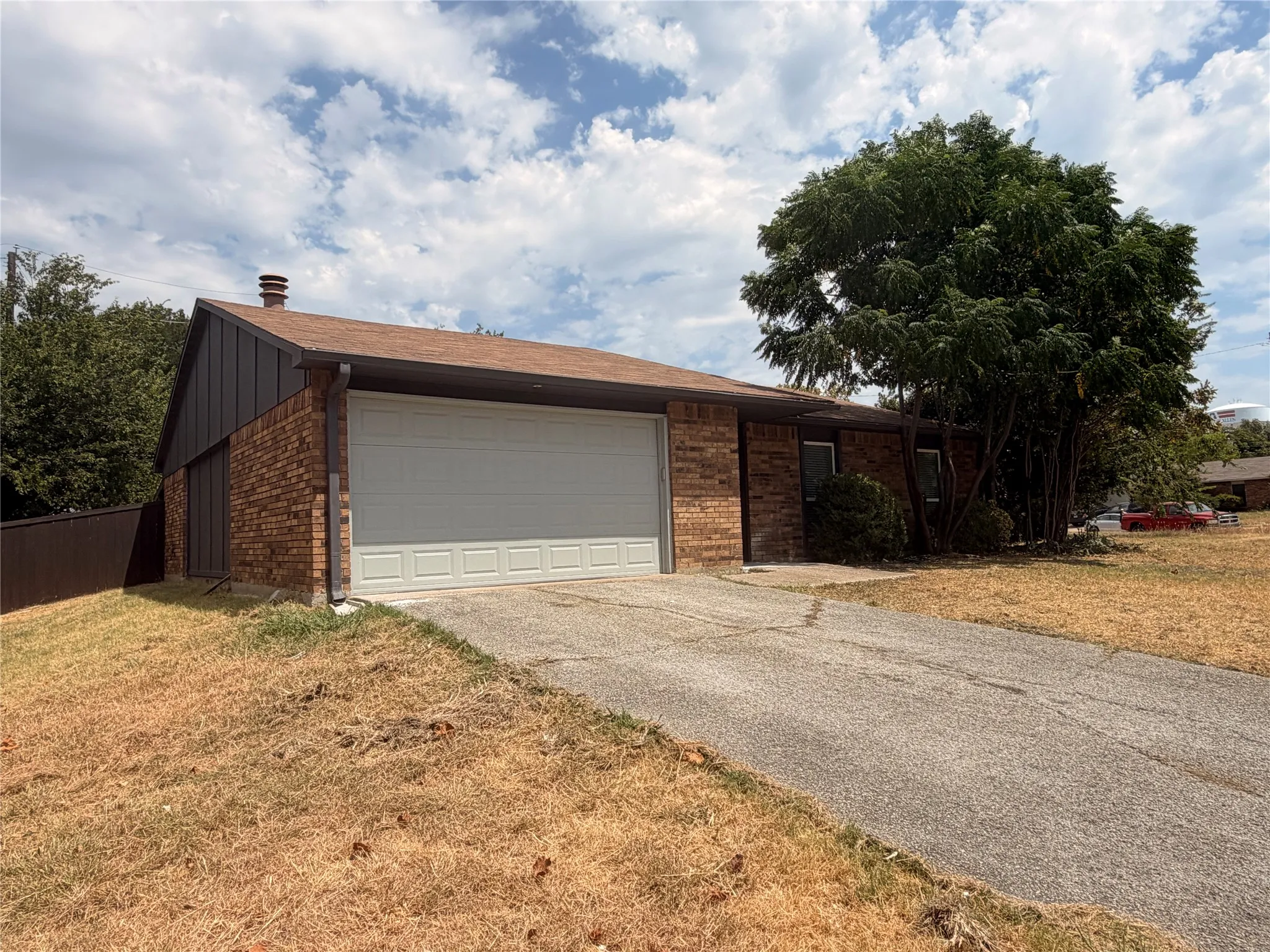 Brick exterior with a peaked roof, attached garage, and mature tree