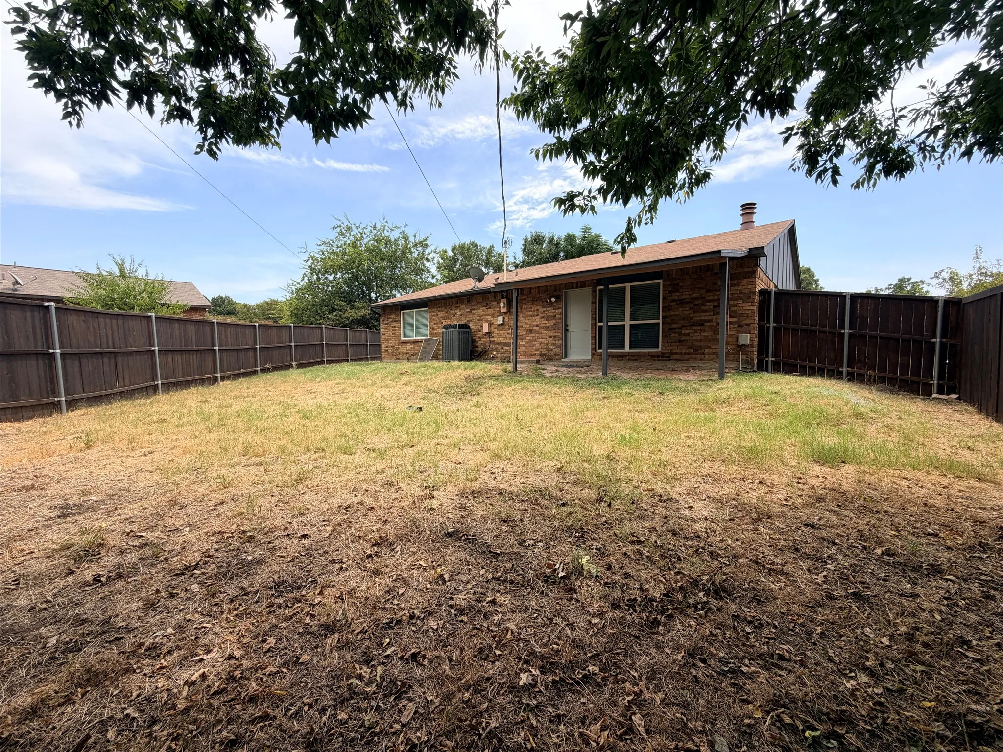 Brick exterior with an attached covered patio, a fenced yard, and a pitched roof