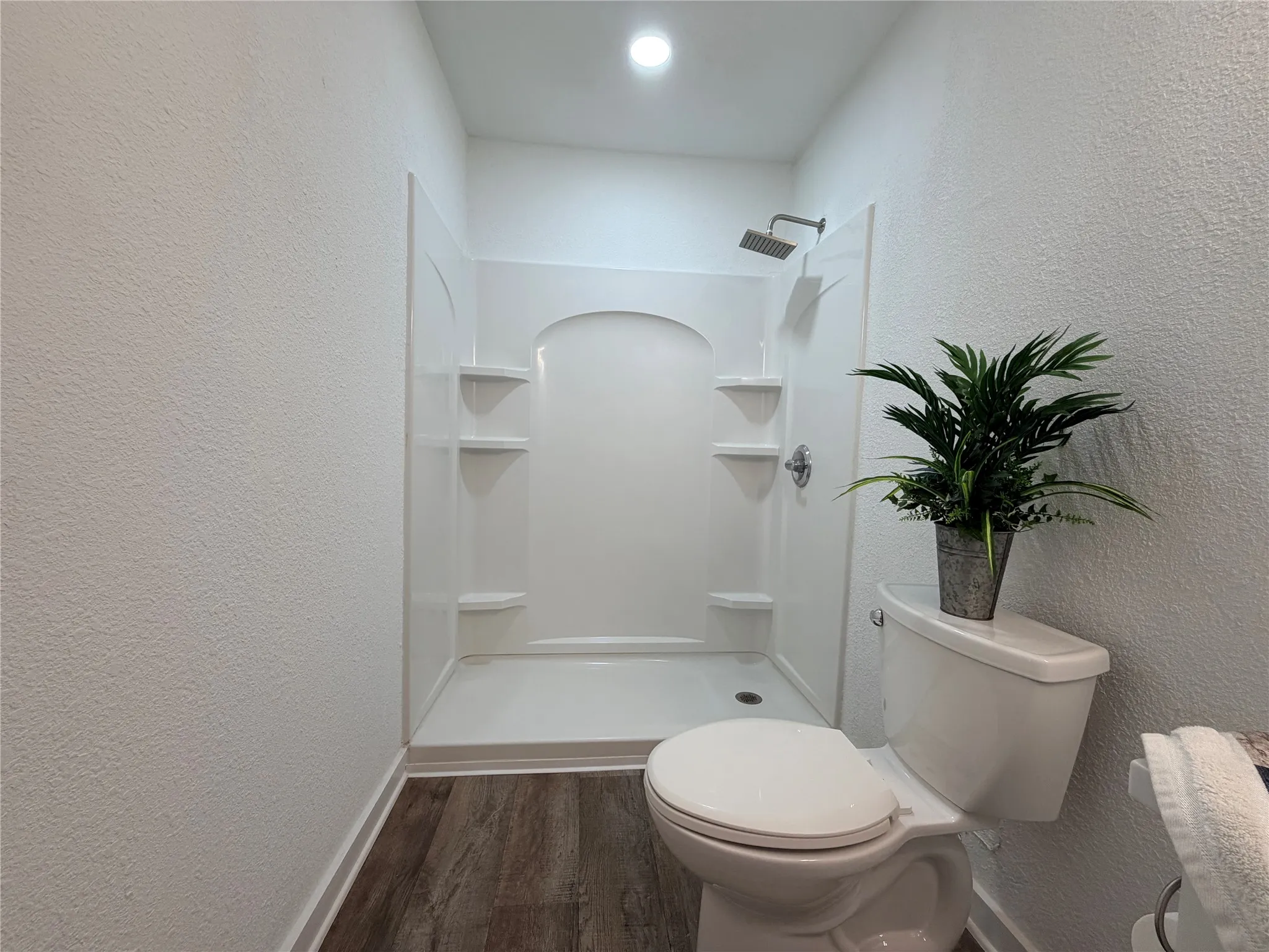 Full shower enclosure with integrated shelving, rainfall showerhead, and wood-finish flooring