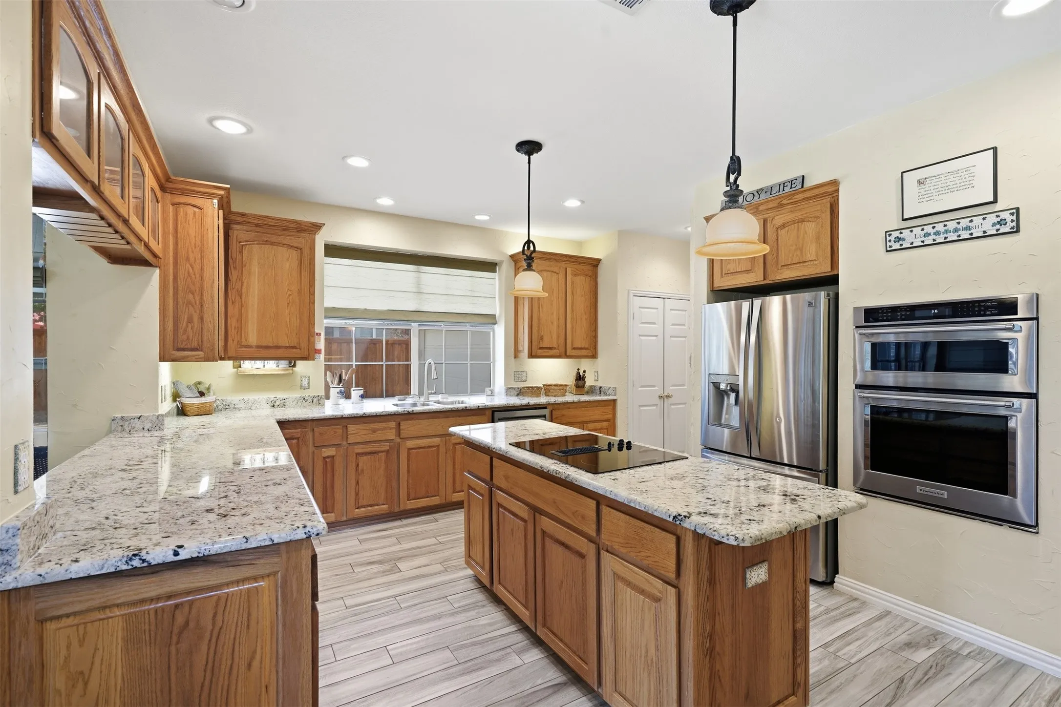 Gourmet kitchen featuring wood cabinetry, light-colored stone countertops, stainless steel appliances, and a central island with a cooktop