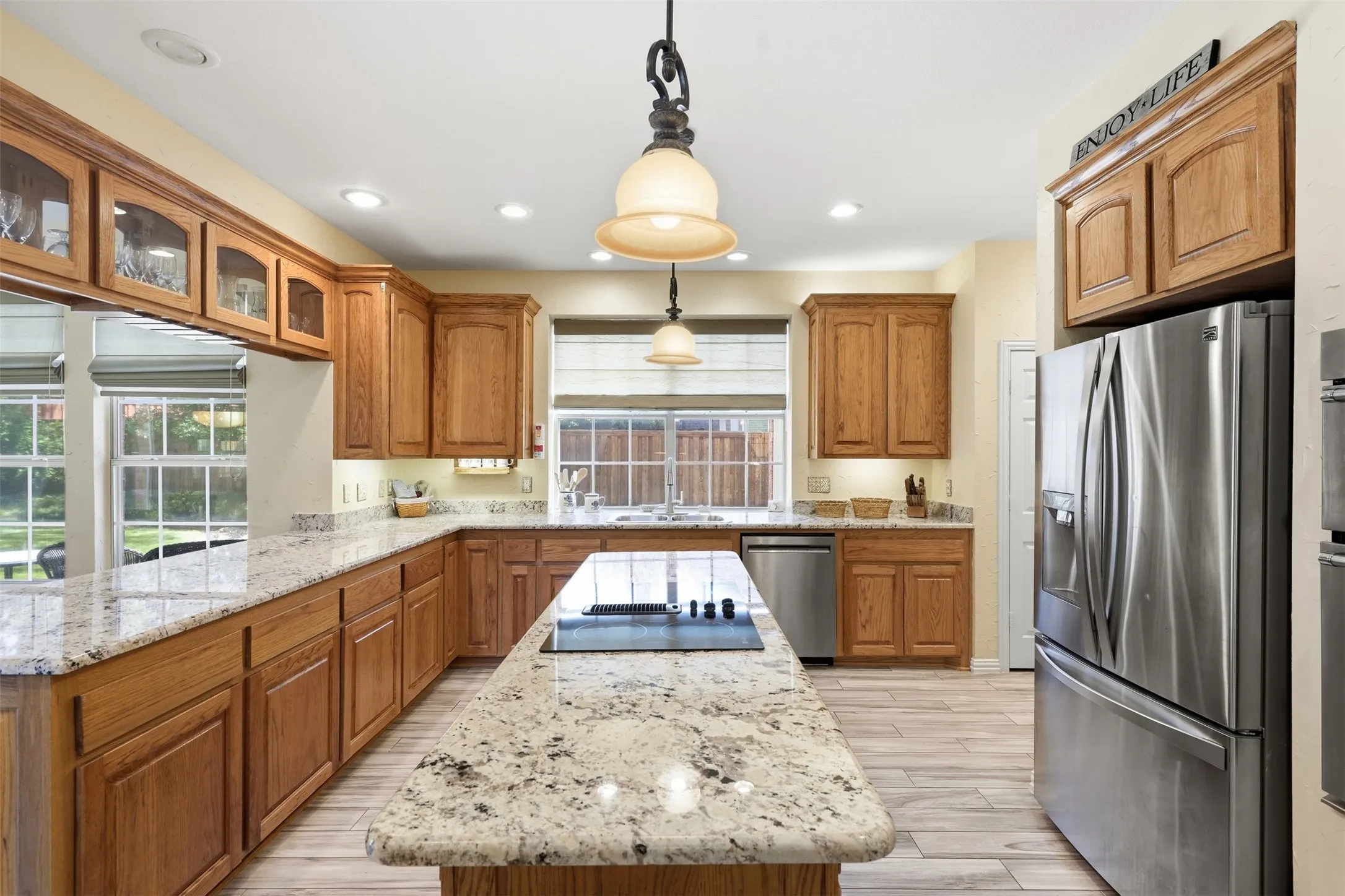 Kitchen featuring light wood cabinetry, granite countertops, a center island with cooktop, stainless steel appliances, and wood-finish flooring