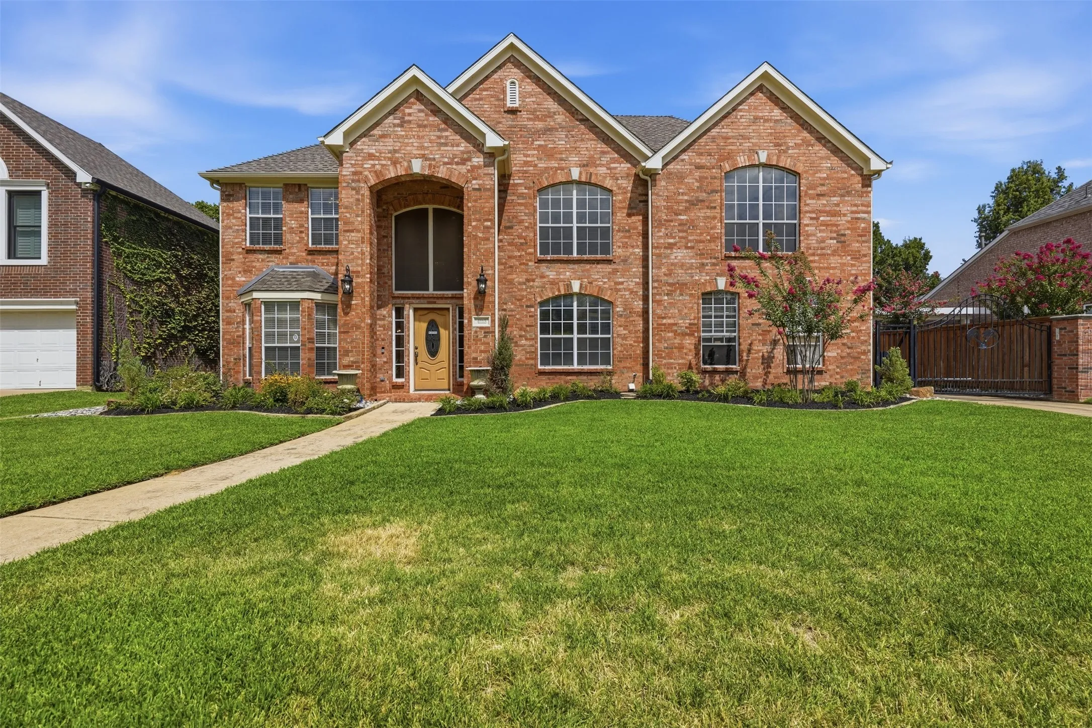 Brick facade residence featuring a prominent arched entry, multiple gabled rooflines, a bay window, and varied window styles including arched and rectangular designs