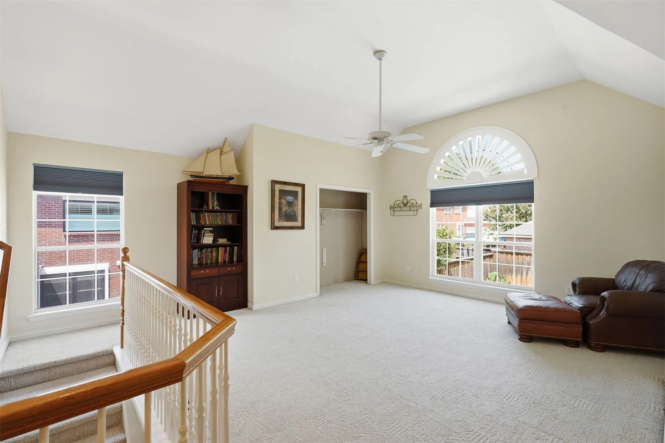 Spacious room featuring vaulted ceilings, light-toned carpeting, a large arched window, and a ceiling fan