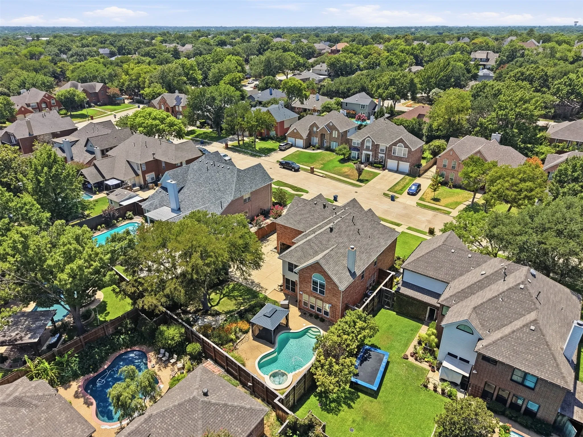 Aerial perspective showcasing a residential neighborhood with numerous homes featuring a variety of architectural styles, mature trees, and private swimming pools