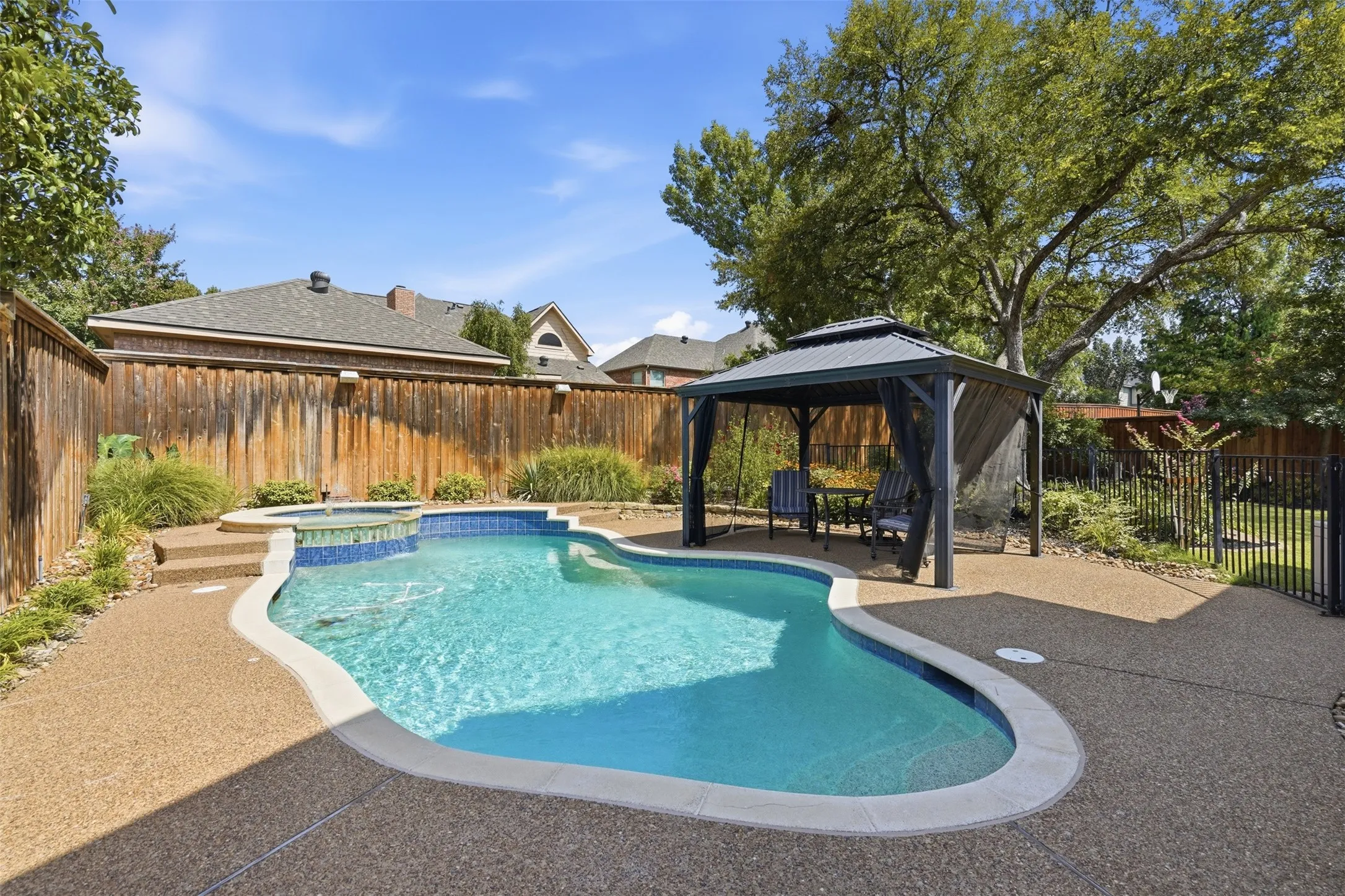 Private backyard oasis featuring a freeform swimming pool with integrated spa and stone steps