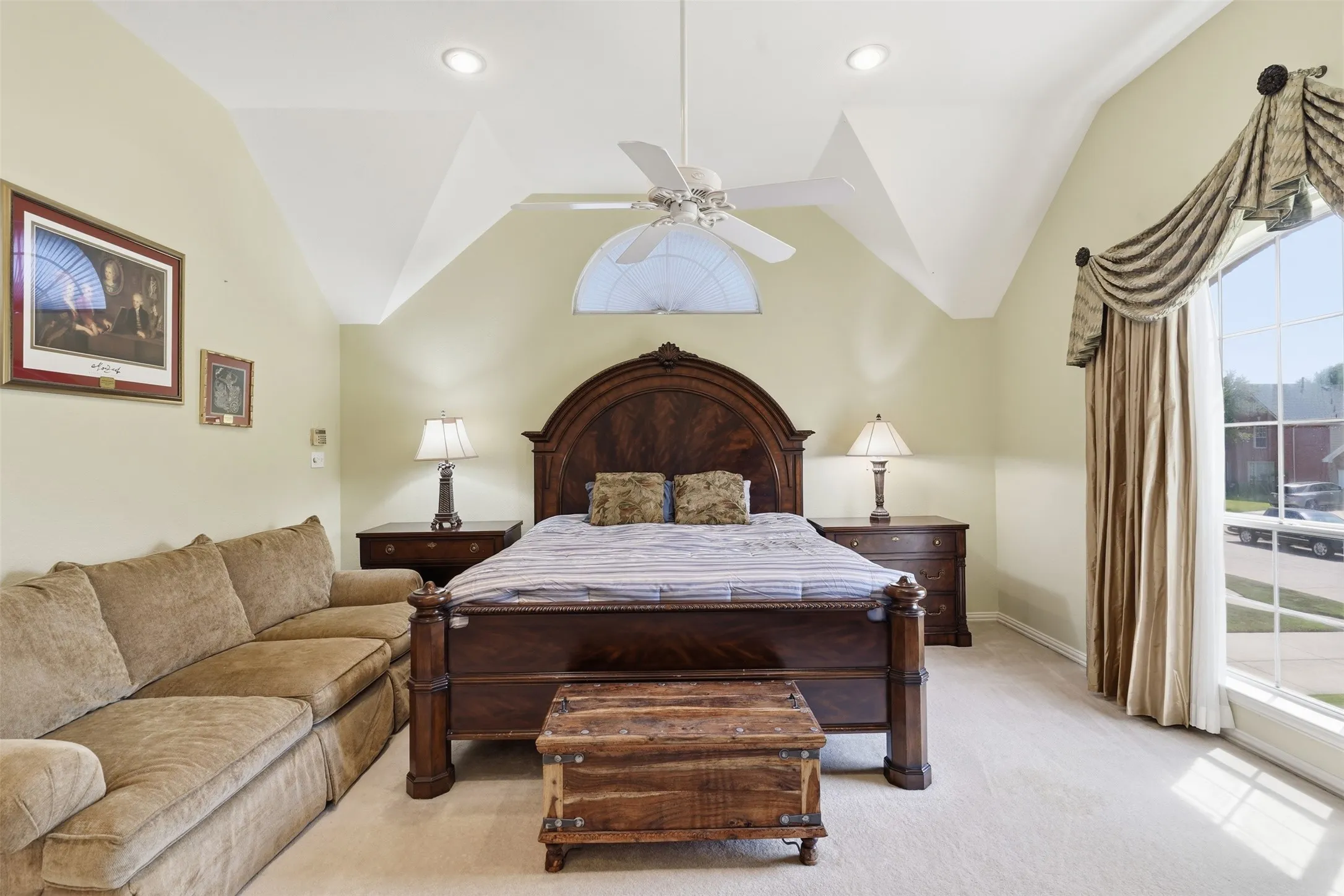 Carpeted room featuring a vaulted ceiling with recessed lighting and a ceiling fan, an arched transom window, and a large arched window with custom window treatments
