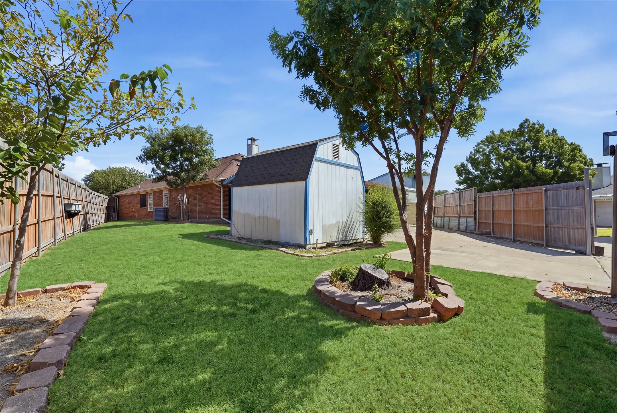 Expansive grass lawn with a storage shed, wood fencing, concrete driveway, and mature trees