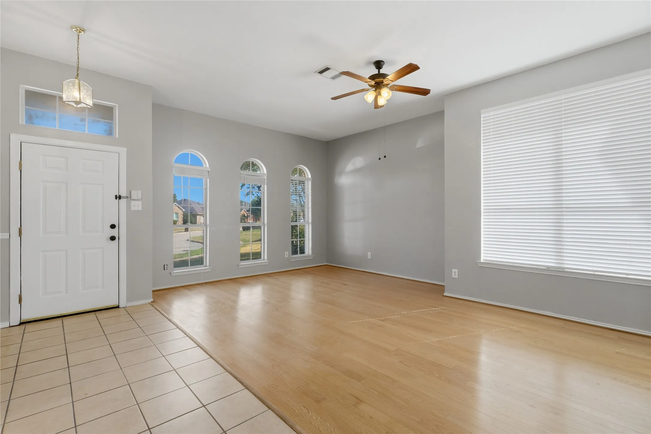 Wood-finish flooring, three arched windows, a rectangular window with blinds, a ceiling fan, and a tile entry