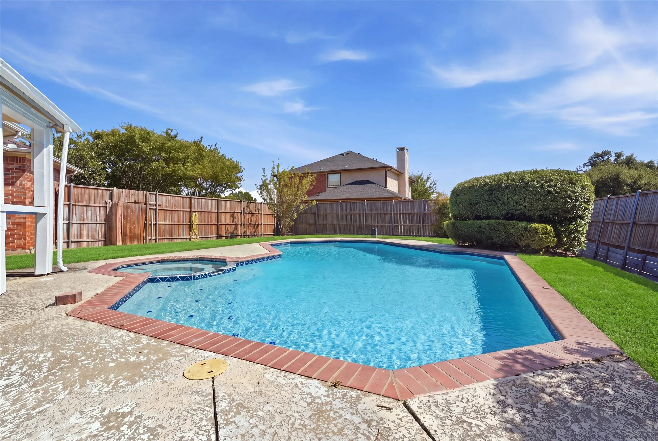 Swimming pool with integrated spa, concrete decking, brick coping, and a surrounding lawn area