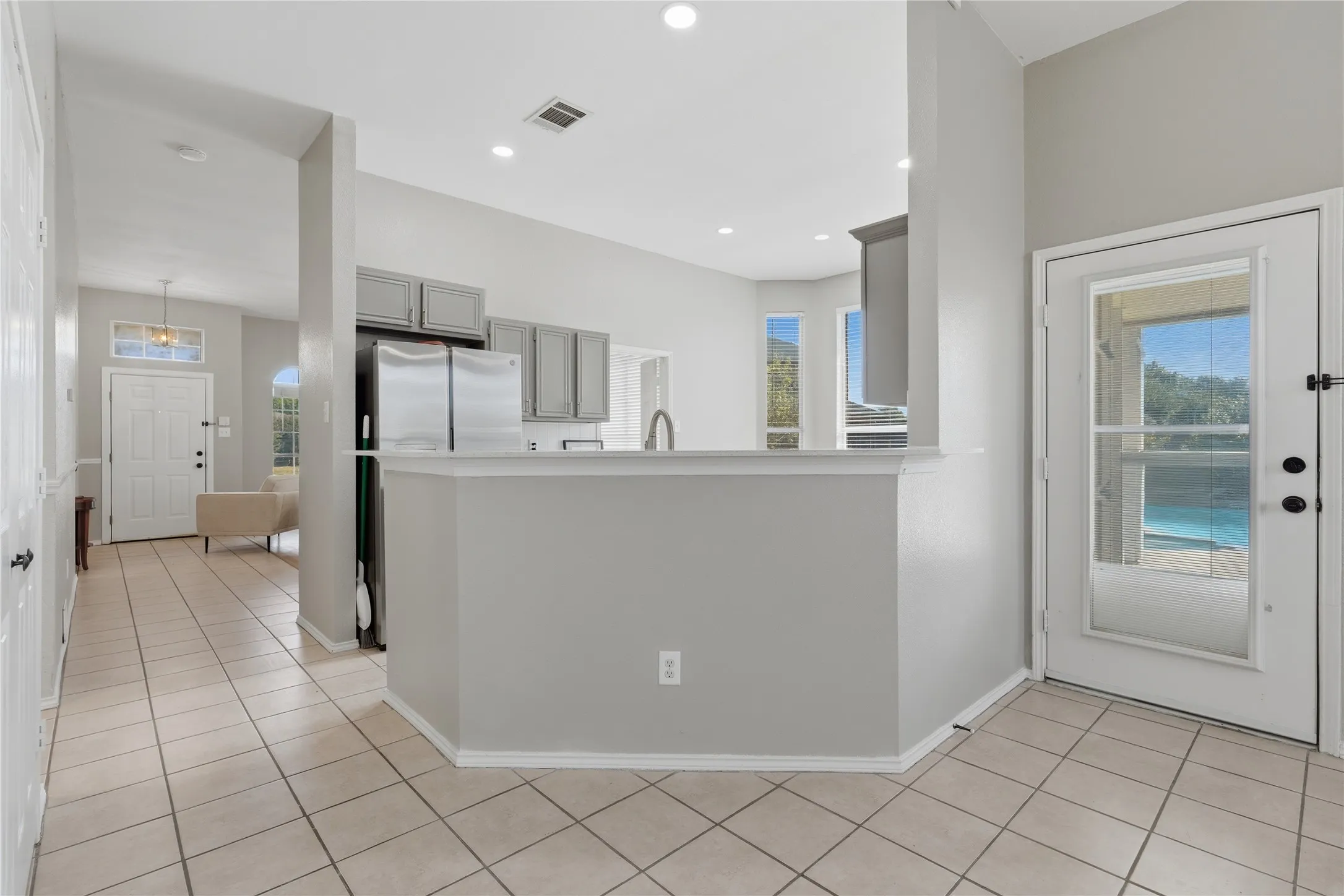 Tiled flooring, recessed lighting, kitchen peninsula, stainless steel refrigerator, white paneled door with glass insert