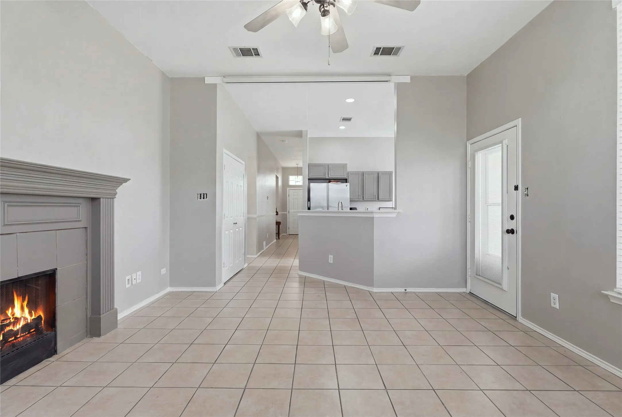 Living area with tile flooring, a fireplace featuring a gray mantel, and a ceiling fan
